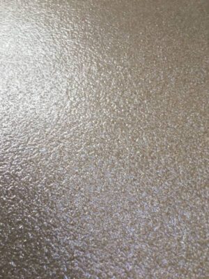 Close-up of a textured grey epoxy floor with a high-gloss finish, exhibiting a slightly mottled appearance with subtle variations in shading. The surface has a granular look, providing both visual interest and slip resistance.