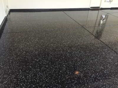 Shiny black epoxy flooring with a dense distribution of small white speckles throughout, reflecting overhead lighting with high gloss.
