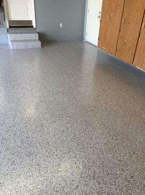 Light grey epoxy floor with fine black speckles throughout the room, complemented by wooden cabinets and a small set of steps leading to a door.