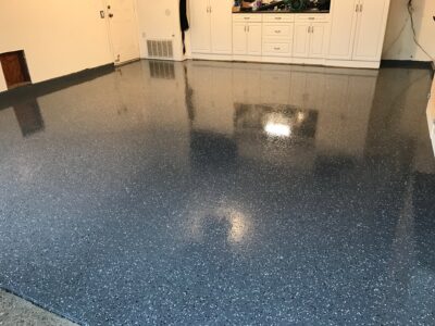 Gleaming dark blue epoxy floor with white speckles in a room, reflecting the ceiling lights and surrounding white cabinetry.