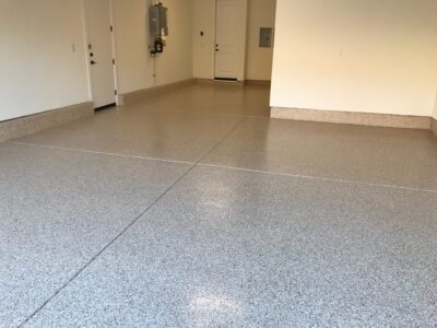 Spacious interior with a light grey and white speckled epoxy floor, showing a clean, bright space with doors and a utility box on the walls.
