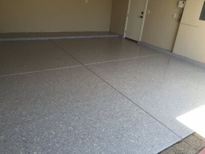 A newly coated speckled epoxy garage floor with a smooth and glossy finish, featuring light grey tones with small black and white flecks, and defined sections created by expansion joints.