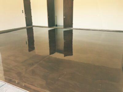 Glossy, translucent brown epoxy floor within a bright room, casting clear reflections of doors and wall edges.