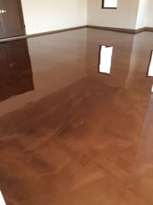 Reflective caramel-colored epoxy flooring in an empty room with natural light streaming in, creating sharp reflections of windows on the surface.