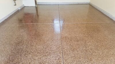 A speckled tan and brown epoxy floor in a room, showing a glossy finish with visible light reflections and a darker stained area.