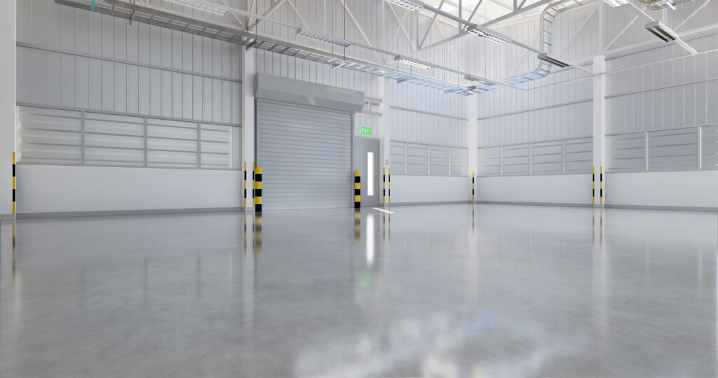 Empty industrial warehouse interior with a high ceiling and multiple closed rolling shutter doors. The doors have translucent panels near the top, allowing for some natural light. The space has a glossy concrete floor reflecting the surroundings, and the walls are adorned with safety markings at regular intervals. Bright LED lights are installed on the ceiling, enhancing the clean and spacious atmosphere. An exit sign is visible above a door, indicating a safety route.