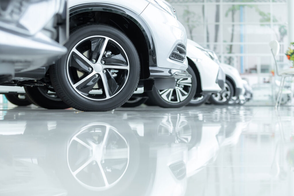 Low-angle view of a lineup of cars in a showroom, focusing on the polished alloy wheels and the reflection on the shiny concrete floor, with bright showroom lighting.