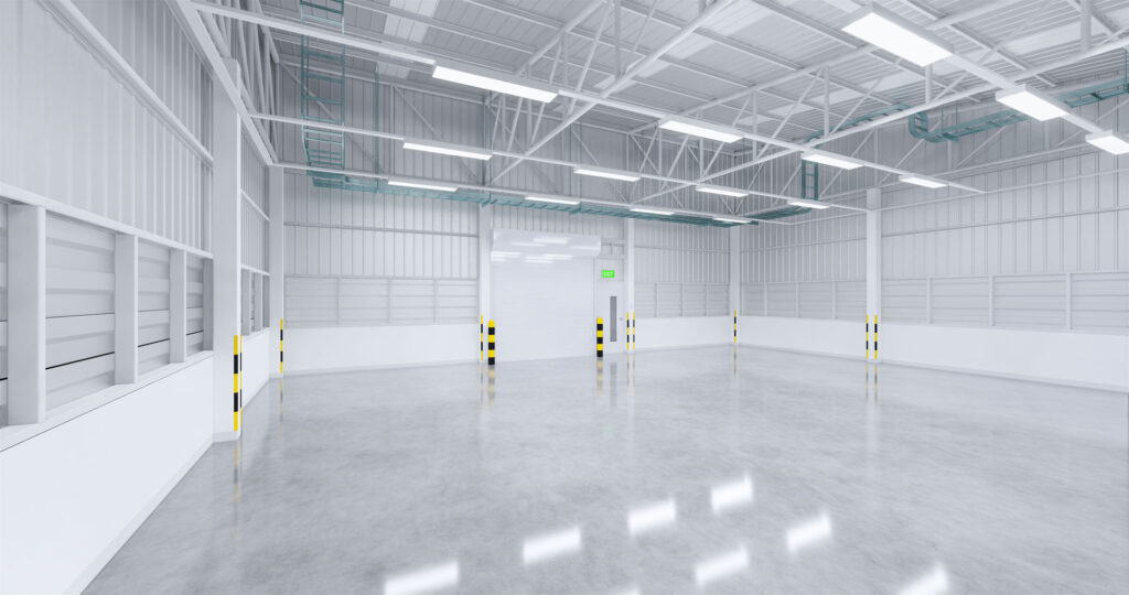Spacious, empty industrial warehouse interior with white walls, high ceiling with skylights, and glossy polished concrete floor reflecting the bright lighting.