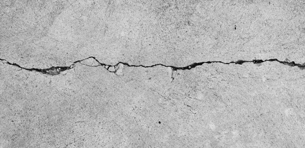 Wide-angle view of a cracked concrete surface with a jagged line running across, showing the rough texture and irregular pattern of the crack.