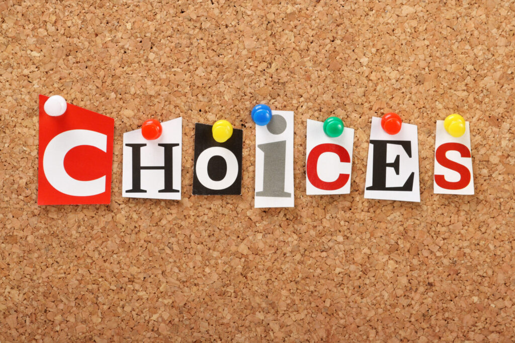 The word 'CHOICES' spelled out with cut-out letters of different fonts, pinned onto a cork board with colorful pushpins referring to the many choices with epoxy coatings.