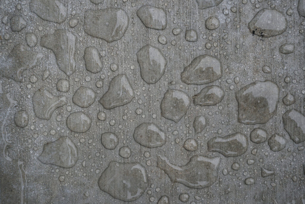 Concrete surface with water moisture droplets of various sizes, creating a textured pattern.