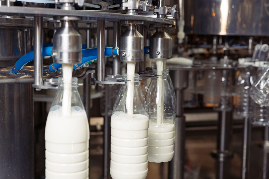 Automated bottling process in a dairy factory with fresh milk being filled into clear plastic bottles, showcasing the industrial machinery and food production line.