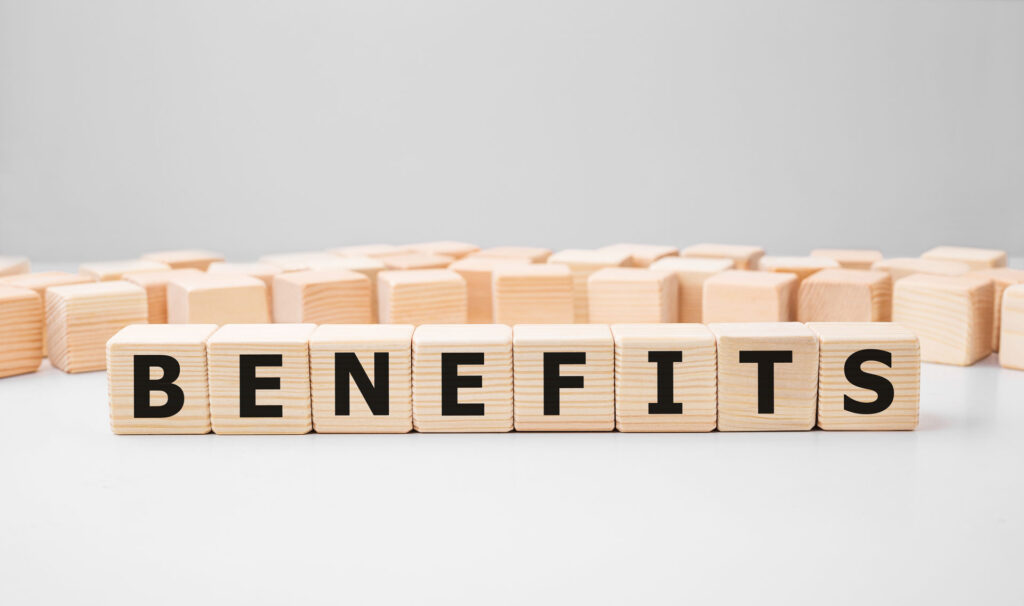 The word 'BENEFITS' spelled out in bold black letters on wooden cube blocks, standing out against a soft-focus background of stacked blocks, on a clean, white surface suggesting the consideration of the benefits of epoxy coatings.