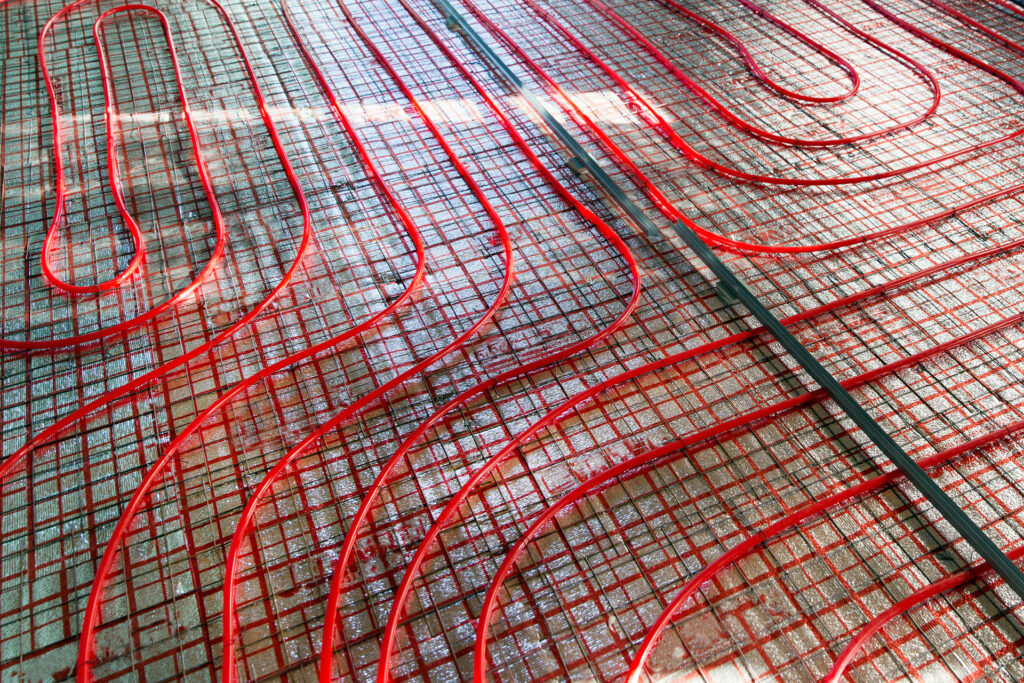 Close-up of a red radiant floor heating heating pipe system installed on a metal grid framework. The pipes create a winding pattern across the floor, indicative of the intricate layout designed to evenly distribute heat throughout the space.