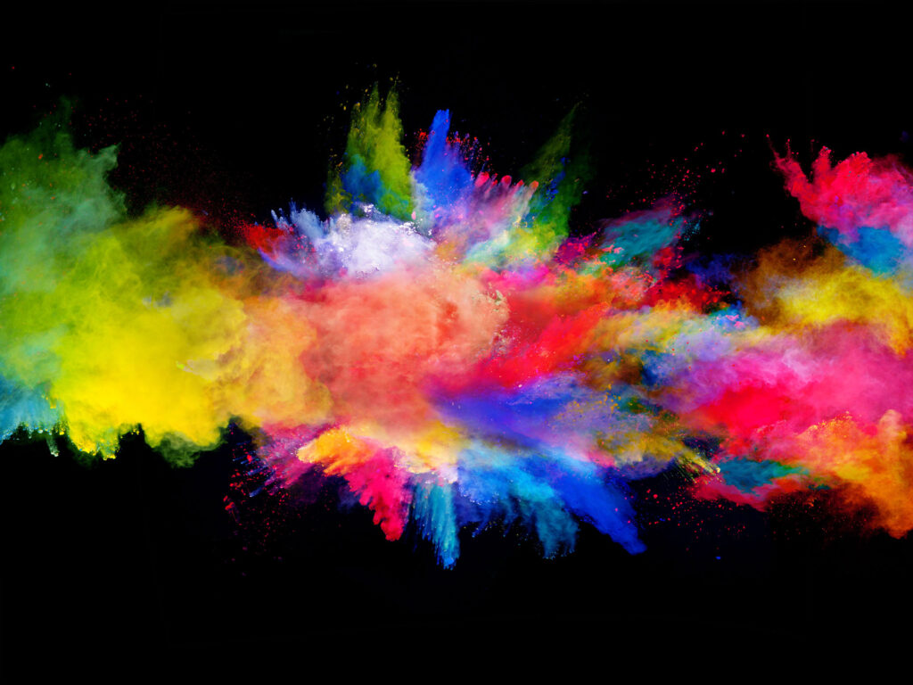 Explosion of vibrant colored powder against a black background, creating a dynamic and abstract burst of yellow, blue, red, and pink hues, resembling a cosmic event or a colorful celebration.