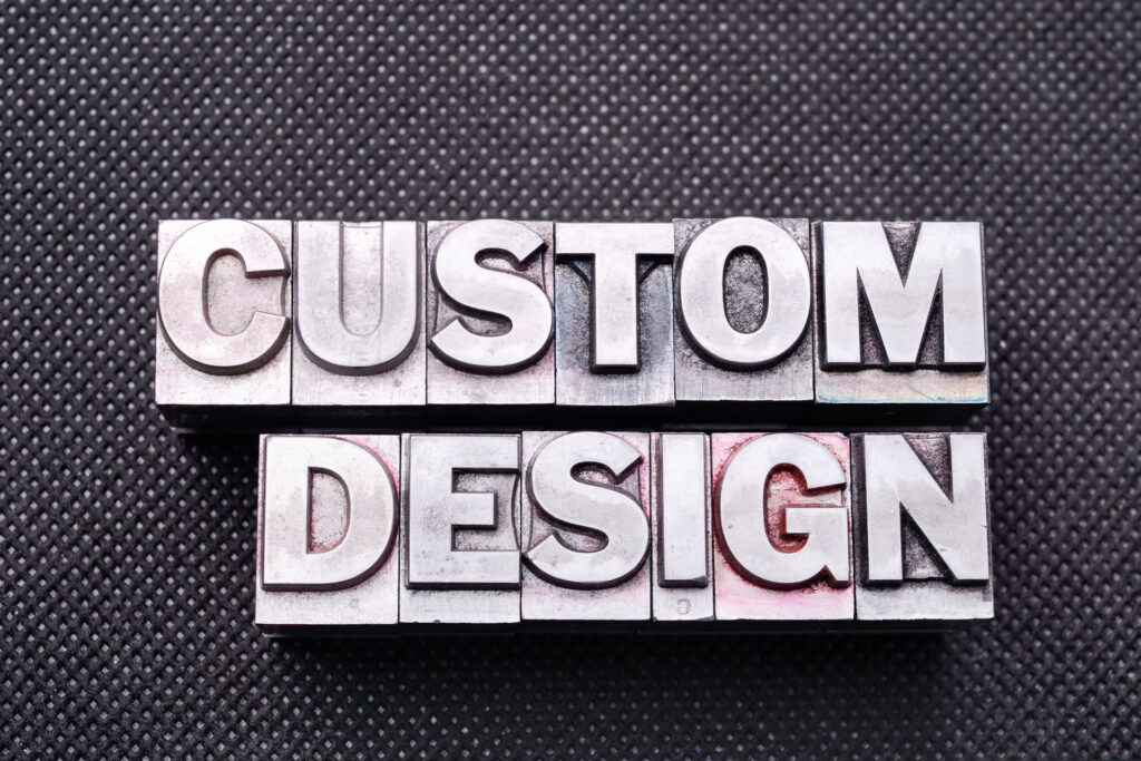 The phrase 'CUSTOM DESIGN' is prominently displayed in uppercase letters using vintage metal letterpress printing blocks on a textured black background, suggesting a theme of bespoke creativity or personalized branding.