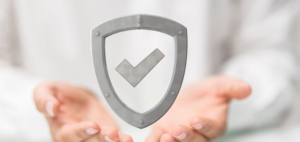Transparent shield icon with a checkmark floating above hands, symbolizing protection, security, and assurance in a white, blurred background.