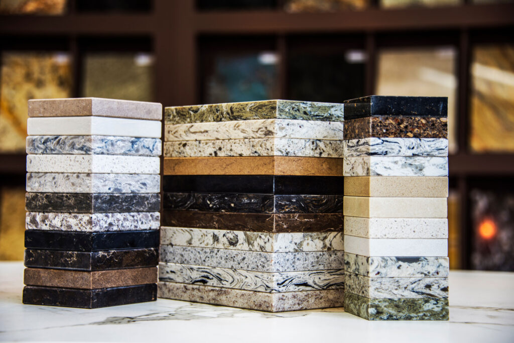 An array of marble samples in various colors and patterns stacked into three columns, displayed against a blurred background featuring a display of additional natural stone options.