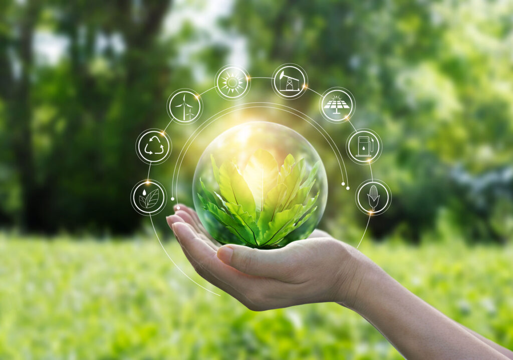 An open hand holding a transparent sphere that encases a vibrant green plant, with icons representing renewable energy, green living, and sustainability floating around it. The backdrop is a lush garden bathed in sunlight, symbolizing the concept of environmental protection and the nurturing of eco-friendly initiatives.