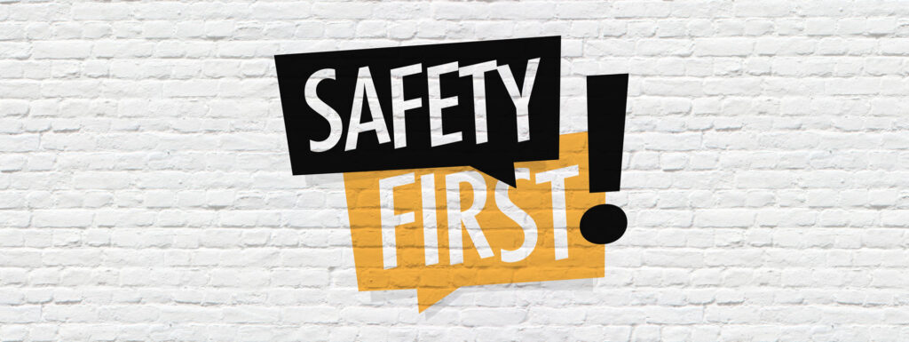 Bold text graphic on a white brick wall background stating 'SAFETY FIRST!' in a dynamic and eye-catching font. The words are black with a striking yellow exclamation point, creating a sense of urgency and importance about workplace safety or precautionary measures.