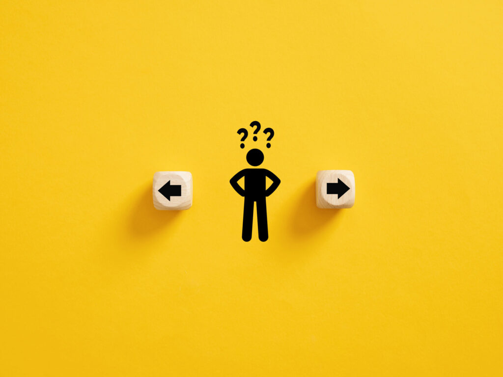 A conceptual image on a bright yellow background showcasing decision-making, with a stick figure standing between two wooden cubes, each pointing in opposite directions with black arrows. Above the figure are question marks, symbolizing the individual's indecision or the process of choosing between two different paths or options such as epoxy coatings or epoxy paint as flooring solutions.