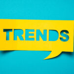 A bold yellow speech bubble cut-out with the word 'TRENDS' in capital letters on a bright turquoise background. The design is simple yet eye-catching, symbolizing trending topics or current popular discussions, ideal for use in articles or sections related to fashion, technology, or social media trends.