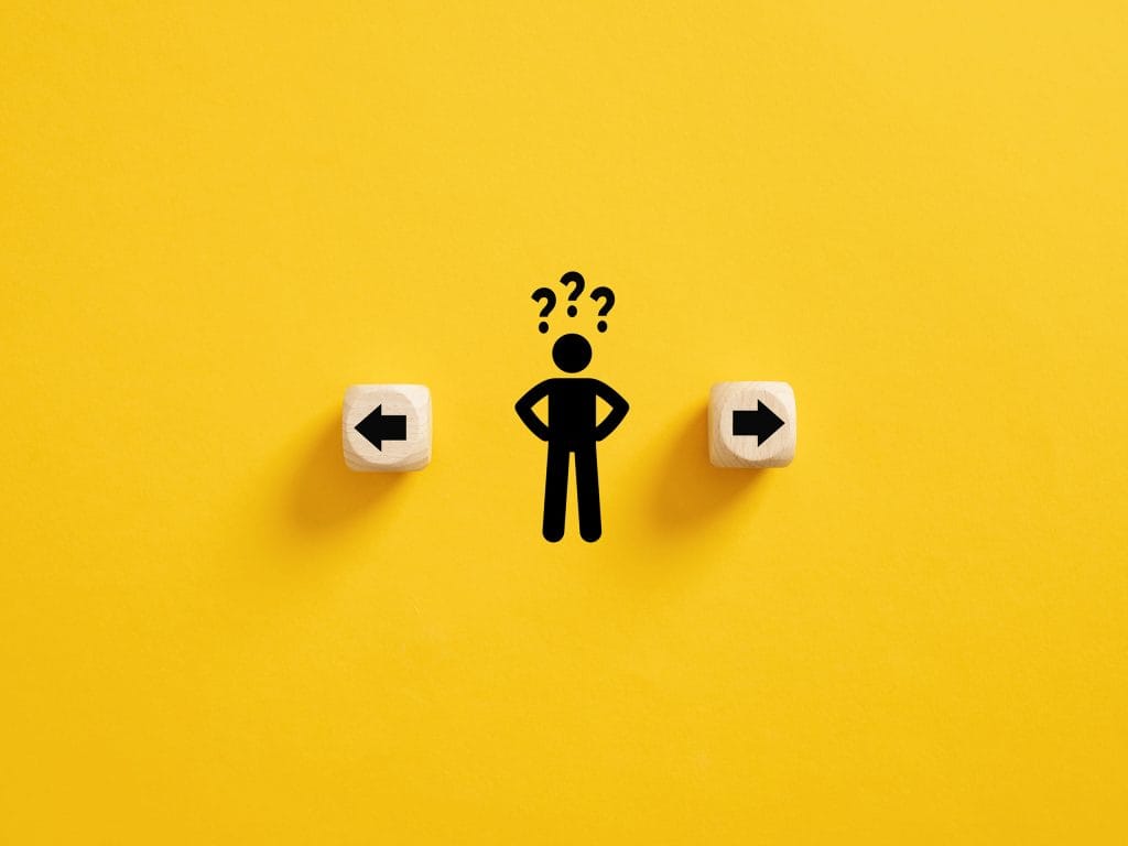 A minimalist illustration of a person icon with question marks above their head, standing between two wooden blocks with arrows. The block on the left shows an arrow pointing left, and the block on the right has an arrow pointing right. The background is solid yellow, emphasizing a sense of decision-making or confusion.