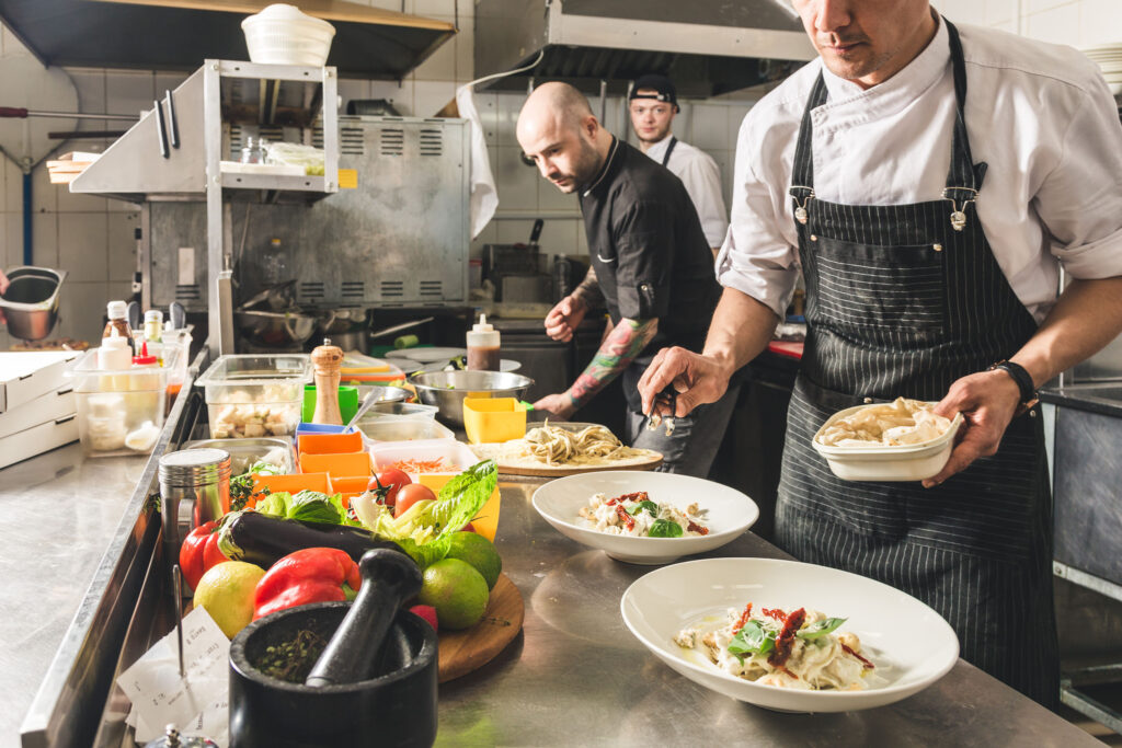 Chefs preparing and plating dishes in a busy commercial kitchen with fresh ingredients on the counter