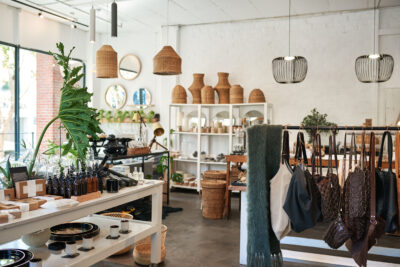Bright boutique interior with shelves of handmade goods, leather bags on a rack, plants, and woven decor in a modern retail space with polished concreted flooring.